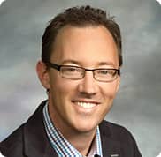 Wood & Delgado | Professional headshot of a smiling male team member wearing glasses and a suit jacket.