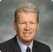 Wood & Delgado | Professional headshot of a middle-aged male executive in a suit and tie against a neutral studio backdrop.