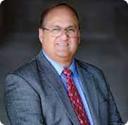 Wood & Delgado | Professional headshot of a male executive wearing glasses, a dark suit, and a red tie.