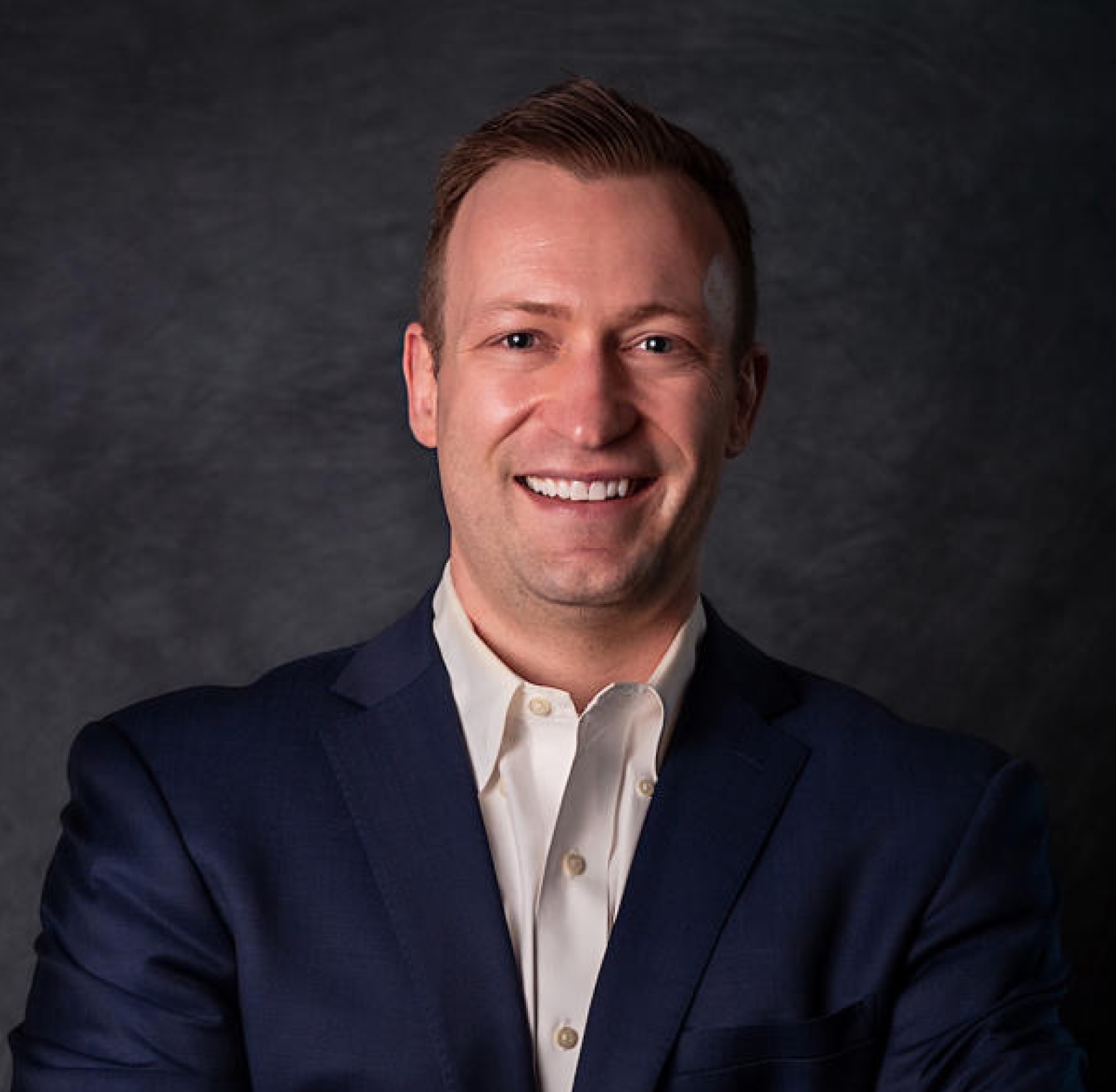Wood & Delgado | Professional headshot of a smiling male team member in a blazer with an outdoor background.